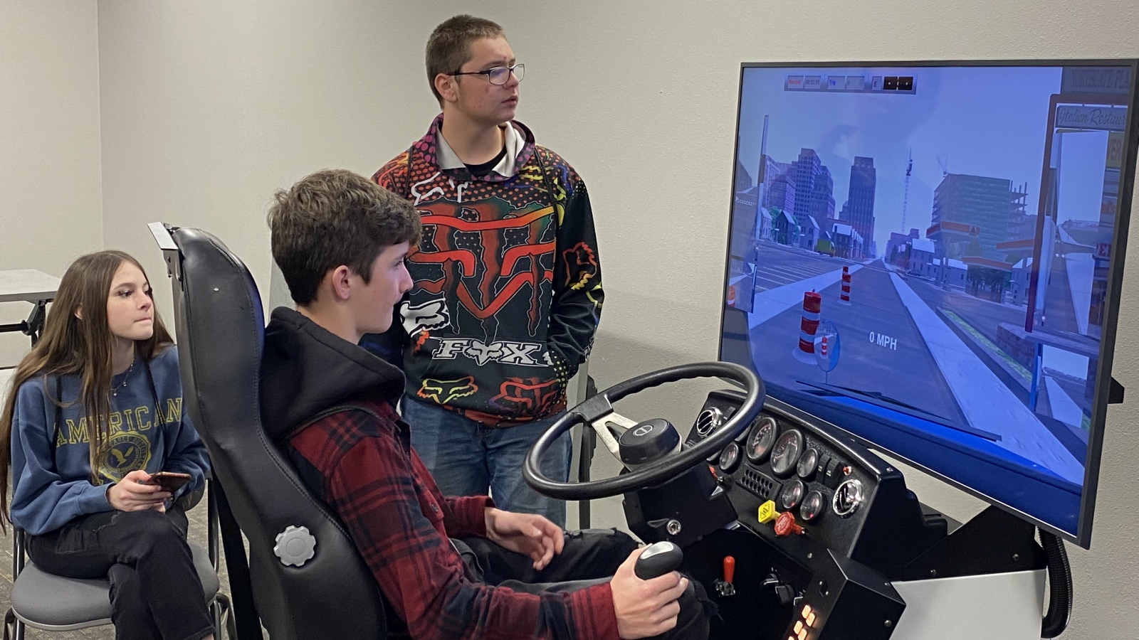 Three Lamar State College Orange students, one using a car driving simulator with the other two watching