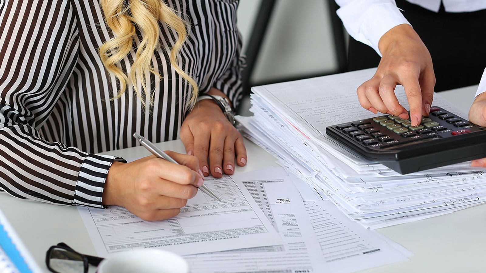 Two individuals hands working with calculator and papers